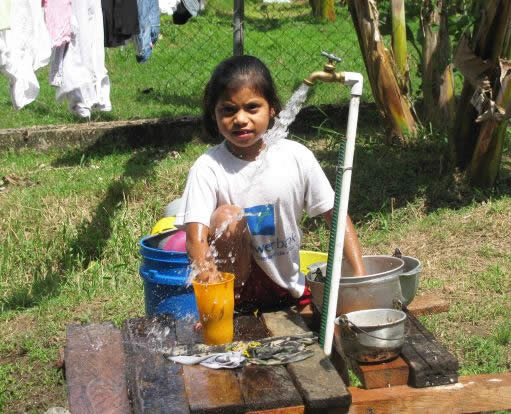 Girl washing dishes at the only water outlet in her community.
